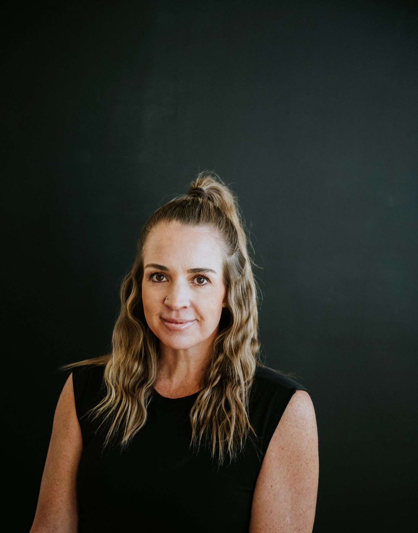 Meg seated against a dark wall, looking calmly into the camera