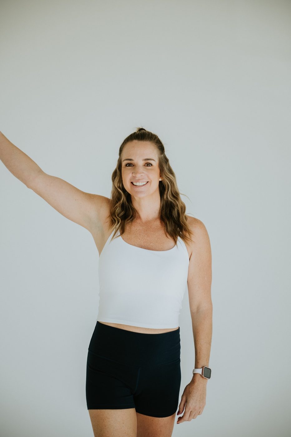 Meg smiling with one arm raised in a bright studio